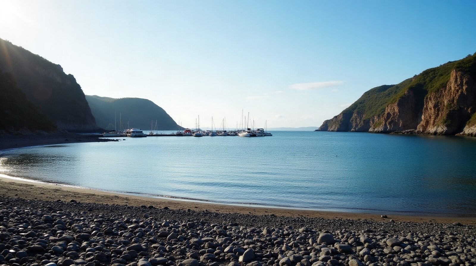 Plage de sable noir et marina avec voiliers au fond d'une anse
